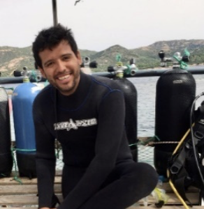 smiling Colombian man with dark hair and a moustache in a black wet suit on a doc